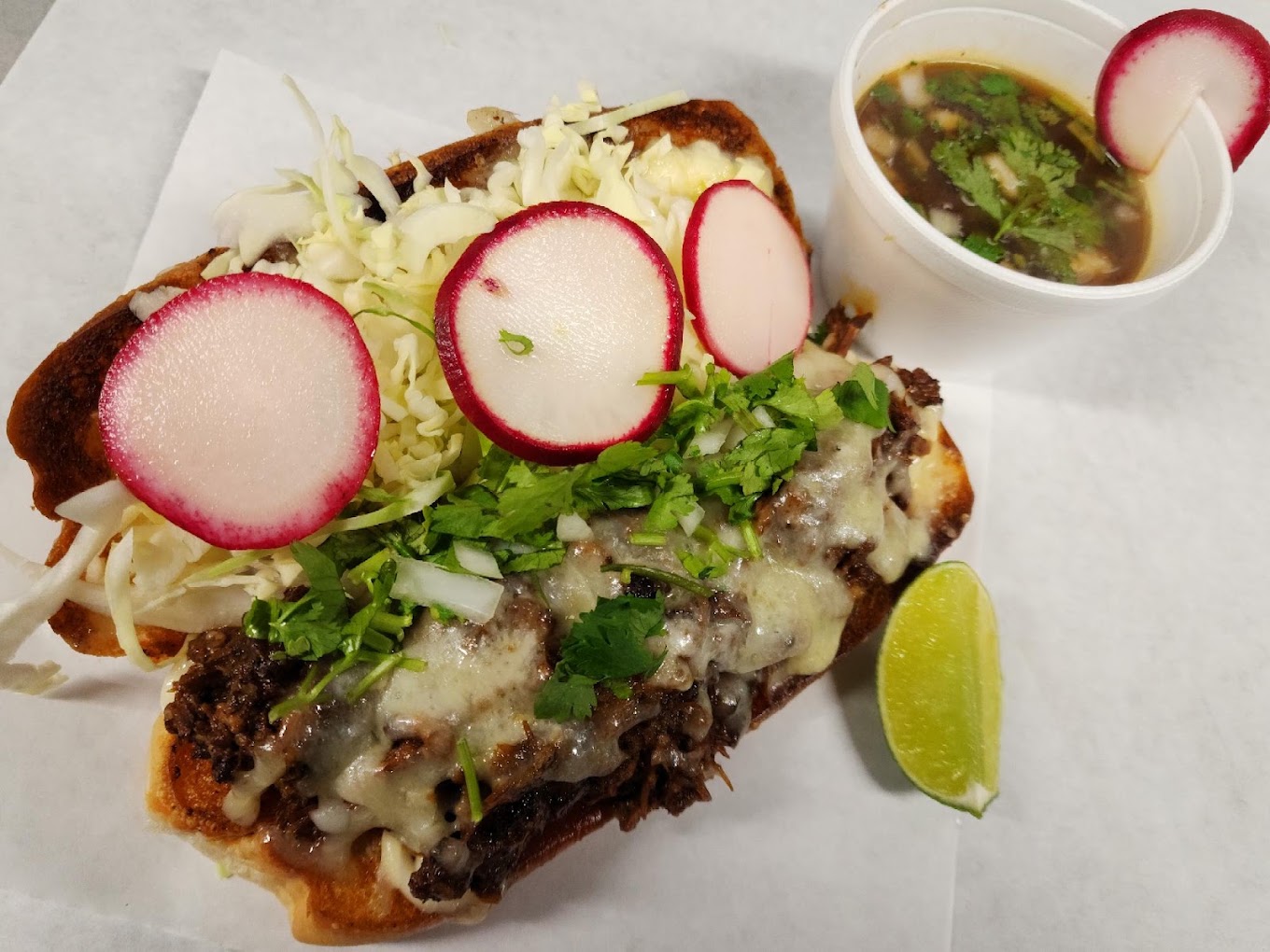 Birria torta with melted cheese, radish and cilantro with a side of consomé