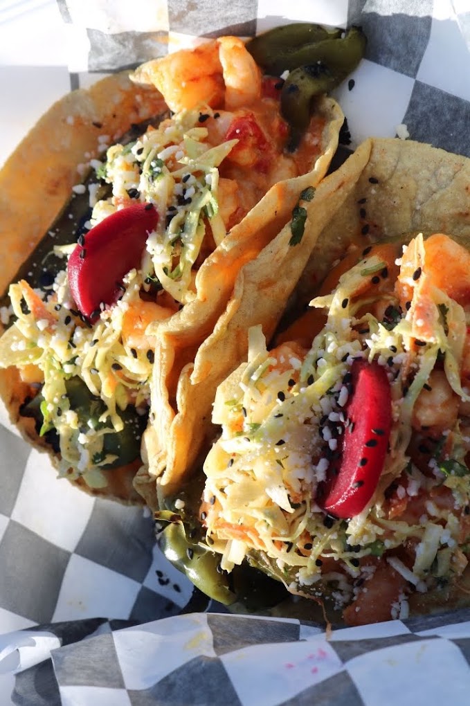 Two shrimp tacos topped with slaw and radish on checkered paper