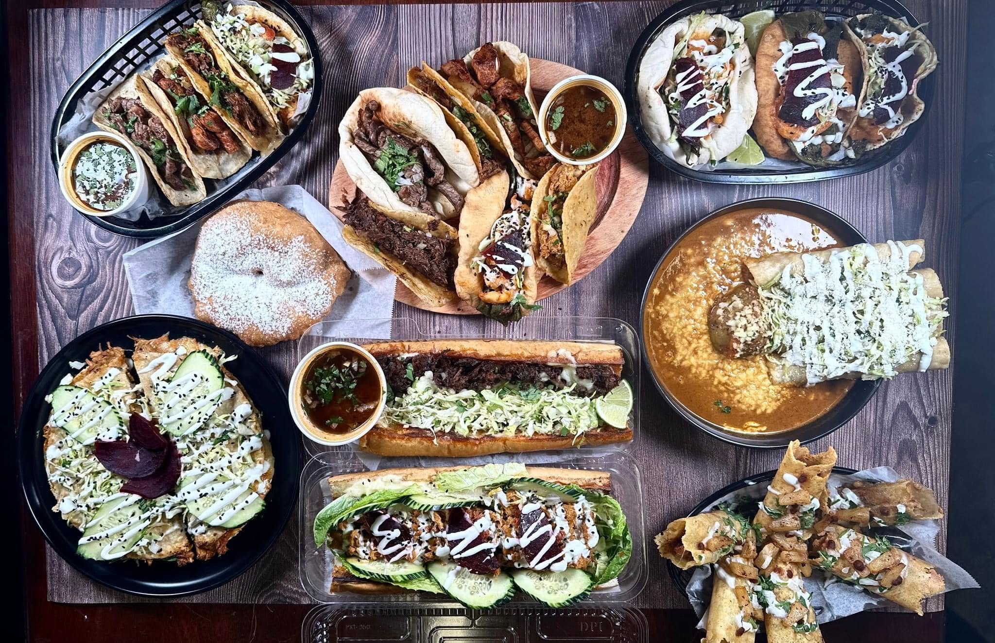 Assorted Mexican dishes including tacos, tortas and flautas on a wooden table