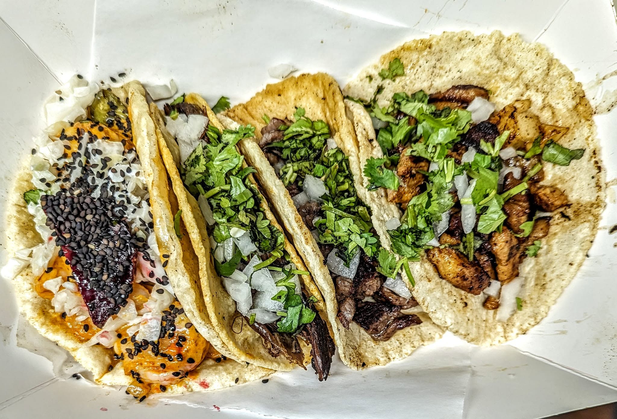 Four street tacos with meat, cilantro, onions and black sesame seeds
