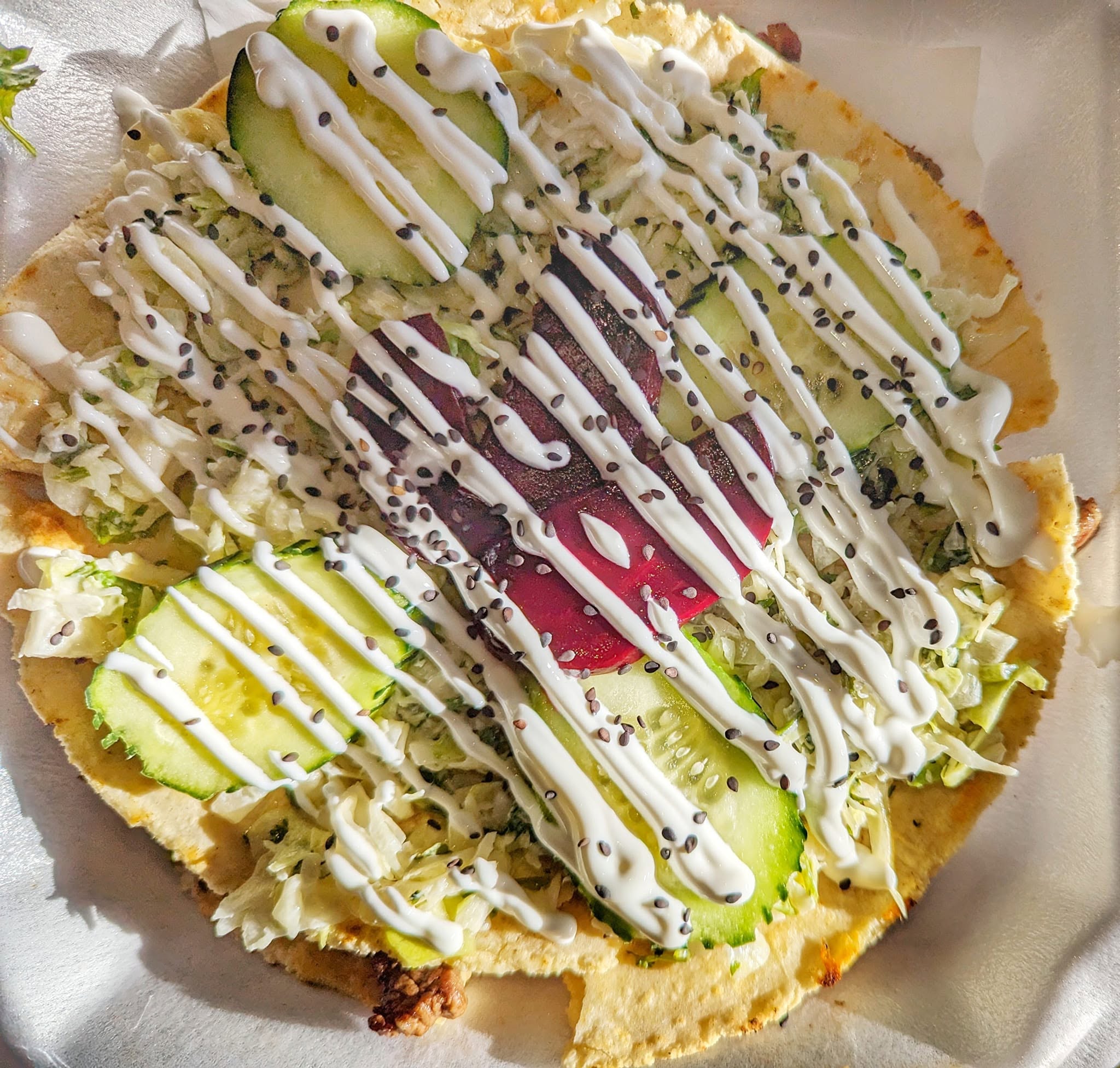 Tostada topped with lettuce, cucumber, beets and crema